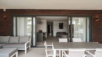 An open-plan living area with a dining table, white chairs, a grey sofa, and a kitchen in the background.