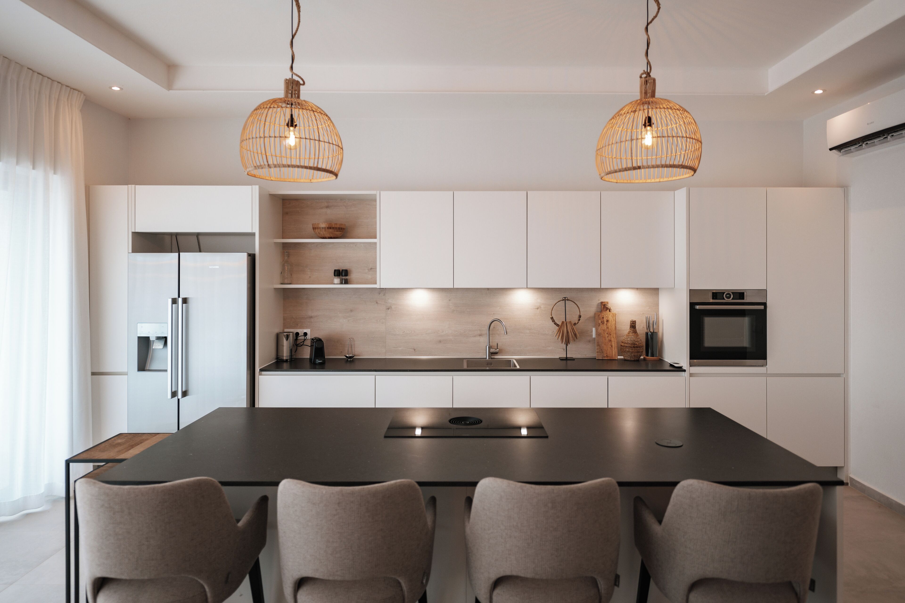 Una cocina moderna con una isla central, armarios blancos e iluminación colgante.