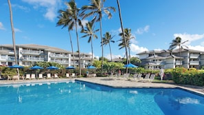 Ein Hotel mit Schwimmbad, Palmen und Liegestühlen.