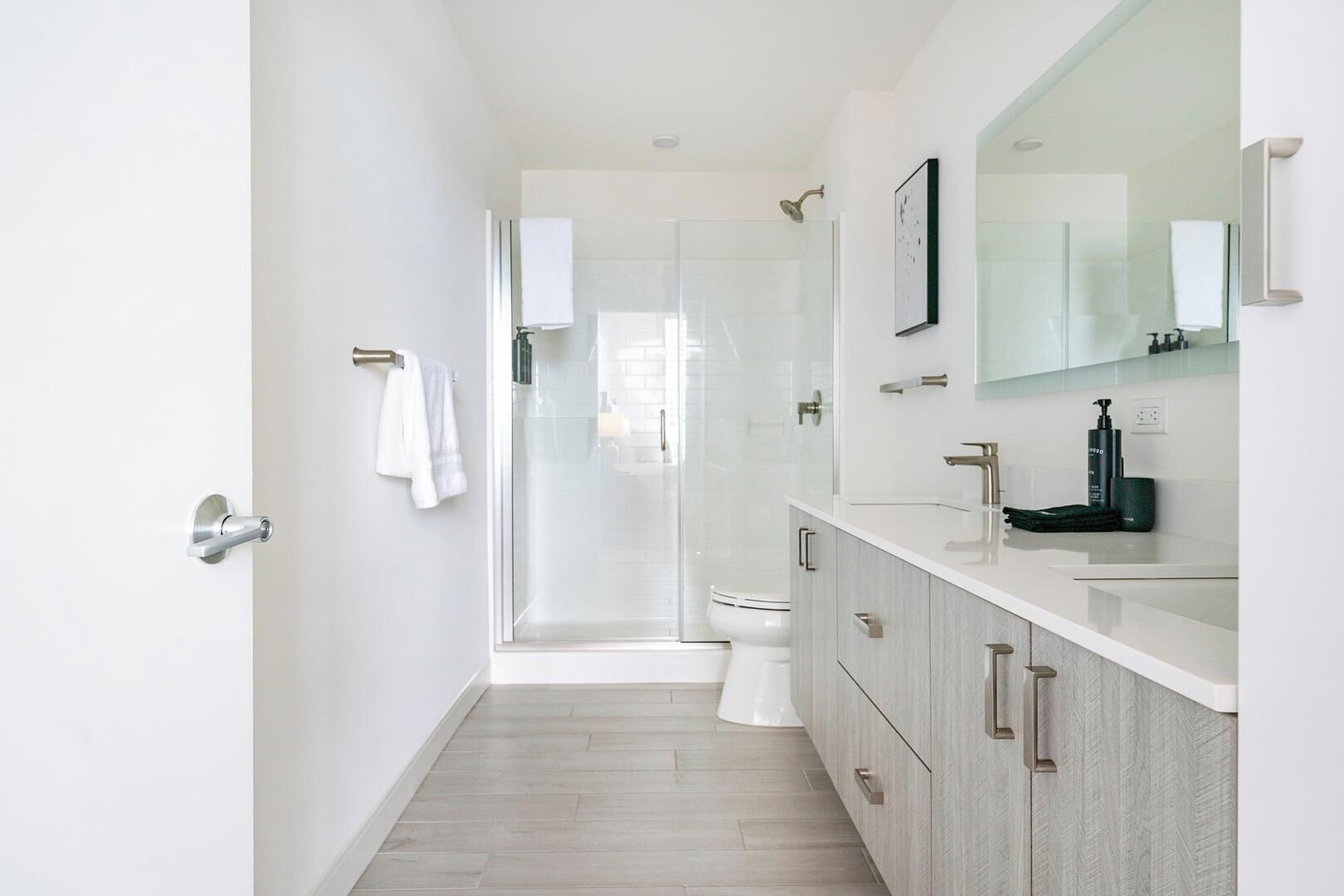 A modern bathroom with a glass shower enclosure, a white toilet, and a vanity with a mirror and sink.