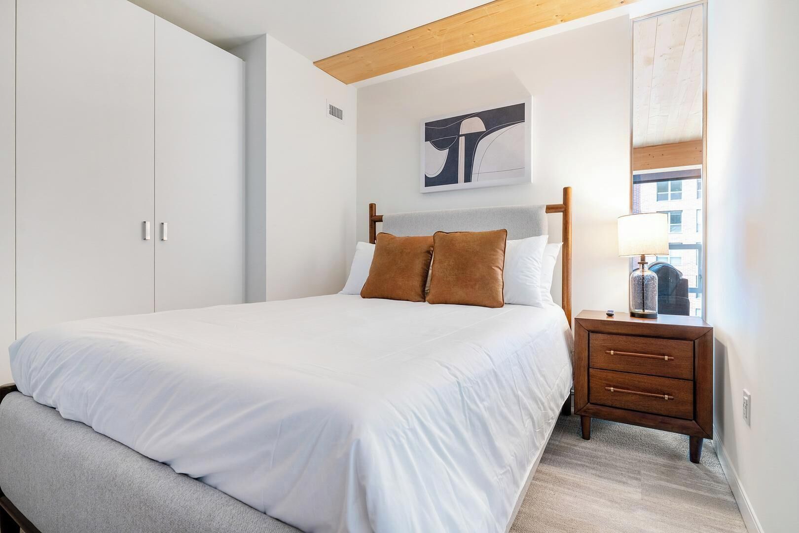 A bedroom with a bed, a nightstand, a wooden headboard, a wall-mounted artwork, and a wardrobe.