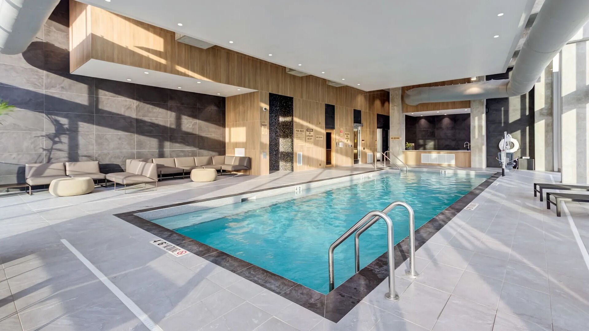 A modern indoor swimming pool with a clear waterline, adjacent seating area, and a poolside bar.