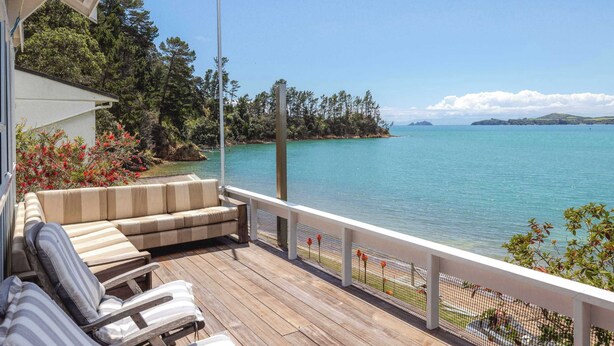 A wooden deck with a sofa and chairs, overlooking a calm lake with a forested island in the distance.