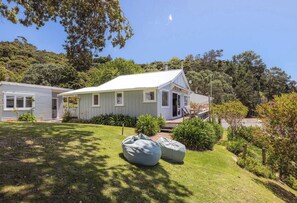 A single-story house with a front porch, a small deck, and a well-maintained lawn. - Barefoot Bach Absolute Waterfront in Arran Bay (Waiheke Island)