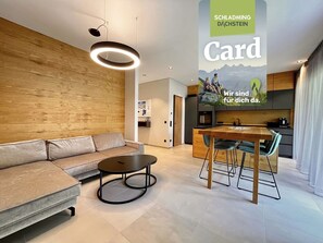 Ein modernes Wohnzimmer mit Sofa, rundem Couchtisch, Esstisch mit Stühlen und einer Küche im Hintergrund.