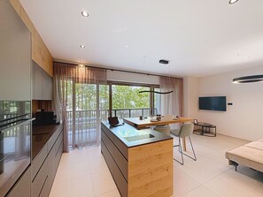 Eine moderne Küche mit einer zentralen Kochinsel, einem Essbereich mit Tisch und Stühlen, einer Couch und einem an der Wand befestigten Fernseher.