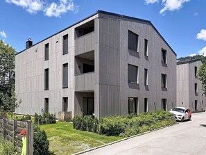 Ein modernes Gebäude mit flachem Dach, mehreren Fenstern und einem sichtbaren Balkon.