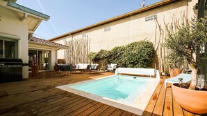 A wooden deck with a swimming pool, outdoor furniture, and a barbecue grill. - Villa Neptune: Family home in the city center (La Teste-de-Buch)
