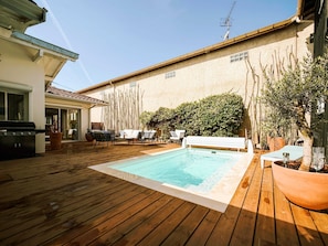 Eine Holzterrasse mit Swimmingpool, Gartenmöbeln und Grill.