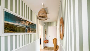 A hallway with striped walls, a hanging wicker light fixture, a framed picture, and a cactus decoration. - Villa Neptune: Family home in the city center (La Teste-de-Buch)