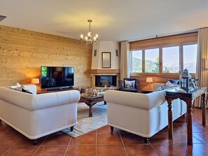 Ein Wohnzimmer mit zwei Sofas, einem Fernseher, einem Kamin, einer Kristallleuchter und einem großen Fenster mit Aussicht.
