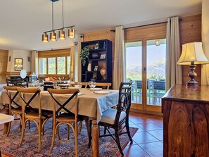 Ein Essbereich mit einem Tisch für vier Personen, Holzsesseln, einer Kandelaber und Blick durch große Fenster.
