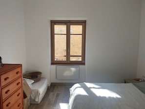 A bedroom with a bed, a dresser, a radiator, and a window with a view.