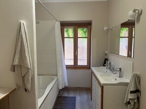 Uma casa de banho com banheira, pia, espelho e janela com vista para vegetação.