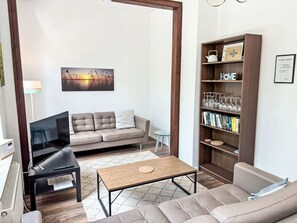 Ein Wohnzimmer mit einer Couch, einem Couchtisch, einem Bücherregal und einem Fernseher.