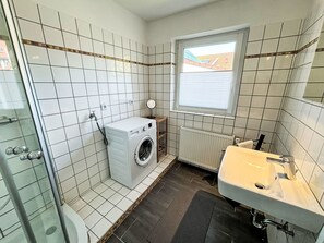 A small bathroom with white tiled walls, a window, a washing machine, a radiator, and a sink. - Wonderful  villa for 6 people with WIFI, TV, terrace and pets allowed (Norden)
