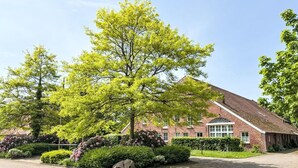 Ein Backsteinhaus mit geneigtem Dach, umgeben von einem gepflasterten Innenhof und üppiger Bepflanzung.