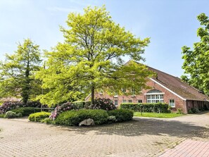 Ein Backsteinhaus mit geneigtem Dach, umgeben von einem gepflasterten Innenhof und üppiger Bepflanzung.