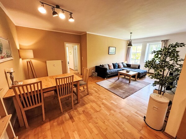 Ein Wohnzimmer mit einer Couch, einem Esstisch mit Stühlen, einem kleinen Couchtisch und einer Topfpflanze.