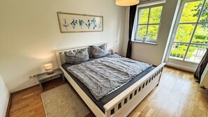 Ein Schlafzimmer mit einem Bett, Nachttischen, einem Teppich, einem Fenster mit Blick auf Grünflächen und einem Wandbild.