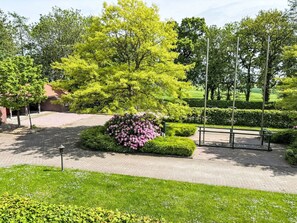 Ein angelegter Garten mit gepflastertem Weg, einem großen Baum und einem Metallzaun.