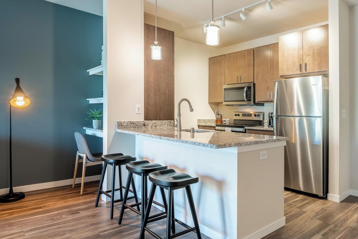 A modern kitchen with a central island, stainless steel appliances, and bar stools.