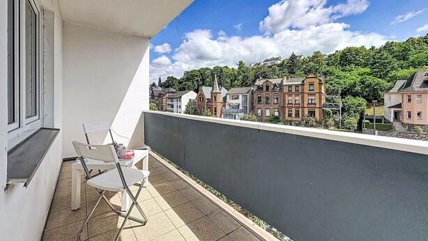 Un balcón con vistas a edificios, una silla y una mesa.
