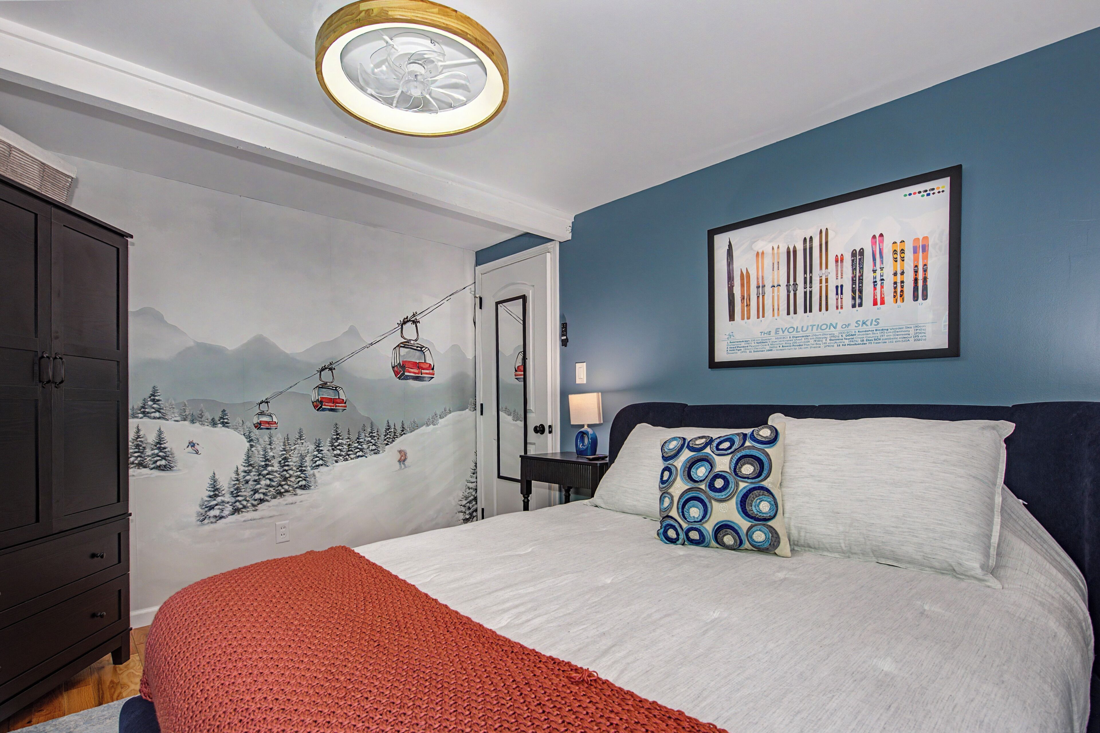 A bedroom with a ski-themed mural, a bed with a red blanket, and a framed picture of skis on the wall.