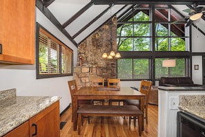 A dining area with a stone wall, wooden table, and chairs, a kitchen with granite countertops, and a ceiling fan. - Escape to St Moritz in the heart of Gatlinburg, where adventure meets comfort in (Gatlinburg)