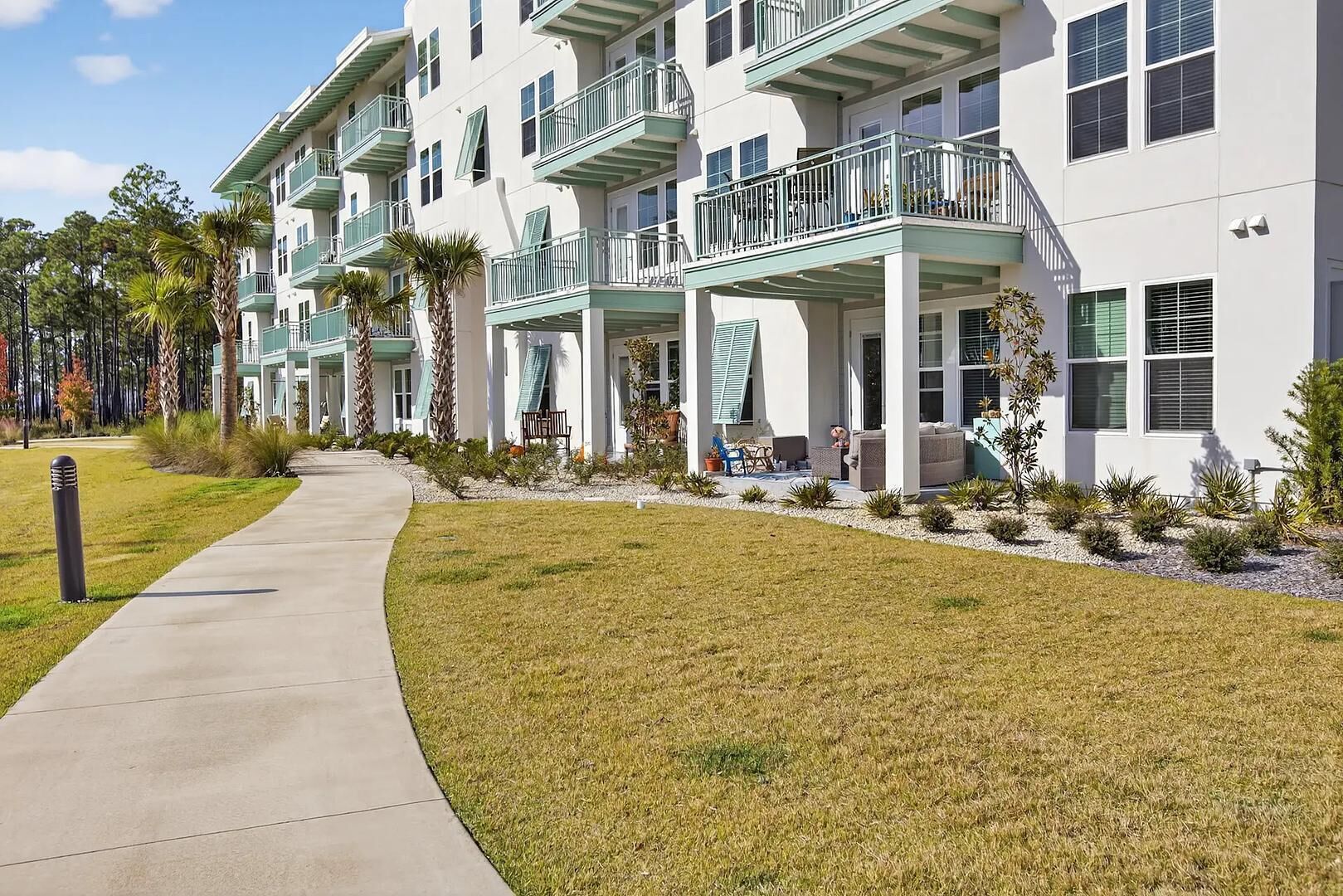 A multi-story hotel with balconies, a covered outdoor seating area, and a well-maintained lawn.