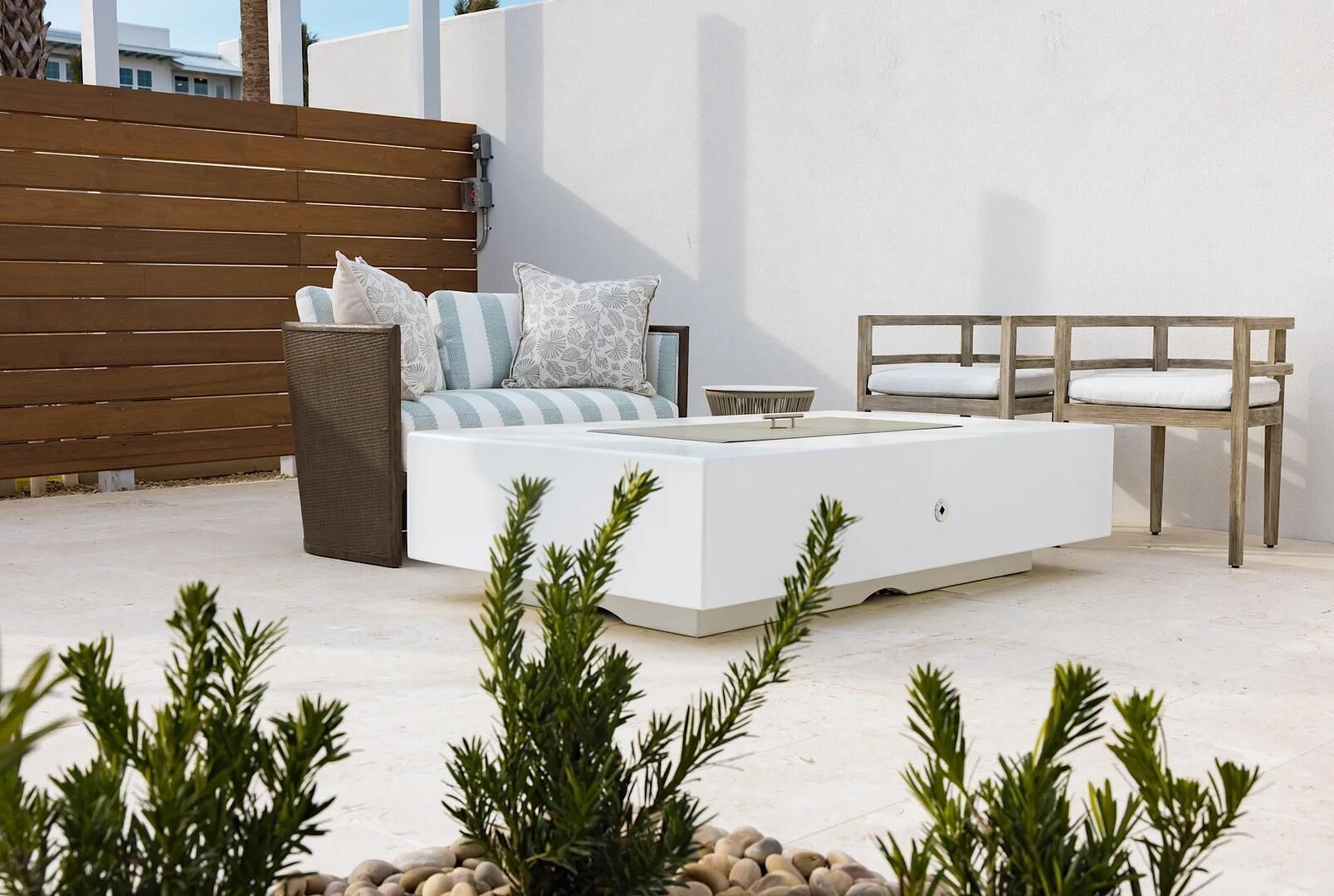 Un espacio exterior moderno con un sofá blanco, cojines y una mesa de madera.