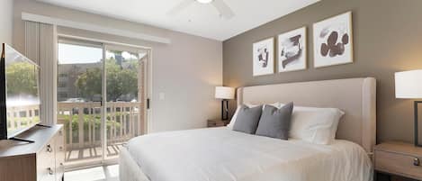 A hotel room with a large bed, a ceiling fan, a TV, and a balcony with a view.