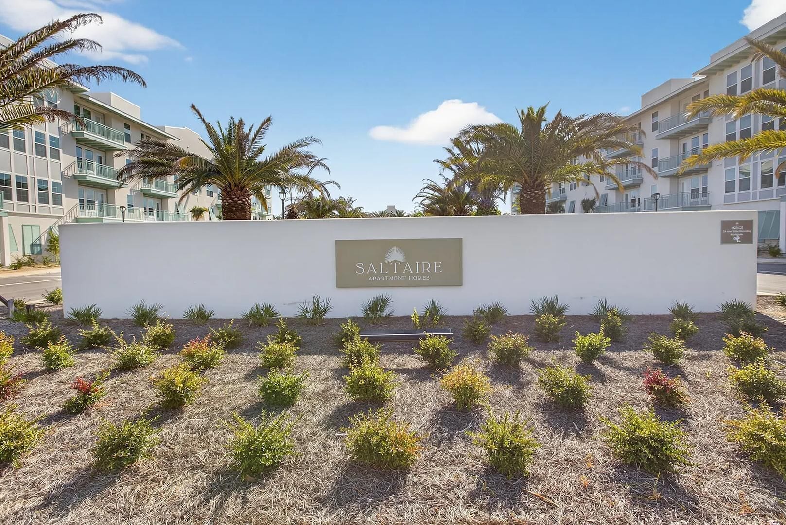 A sign for Saltaire Apartment Homes with a white wall and a row of small plants in front.