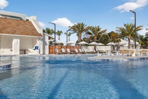 A swimming pool with lounge chairs and umbrellas, surrounded by palm trees and a modern building. - Landing Beautiful 1BD (Santa Rosa Beach)