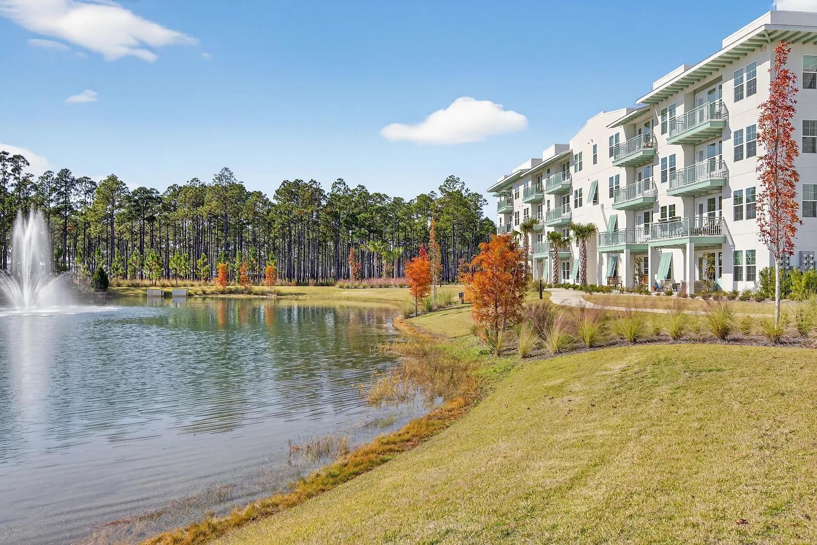 A hotel with a water feature, a lawn, and a row of trees.