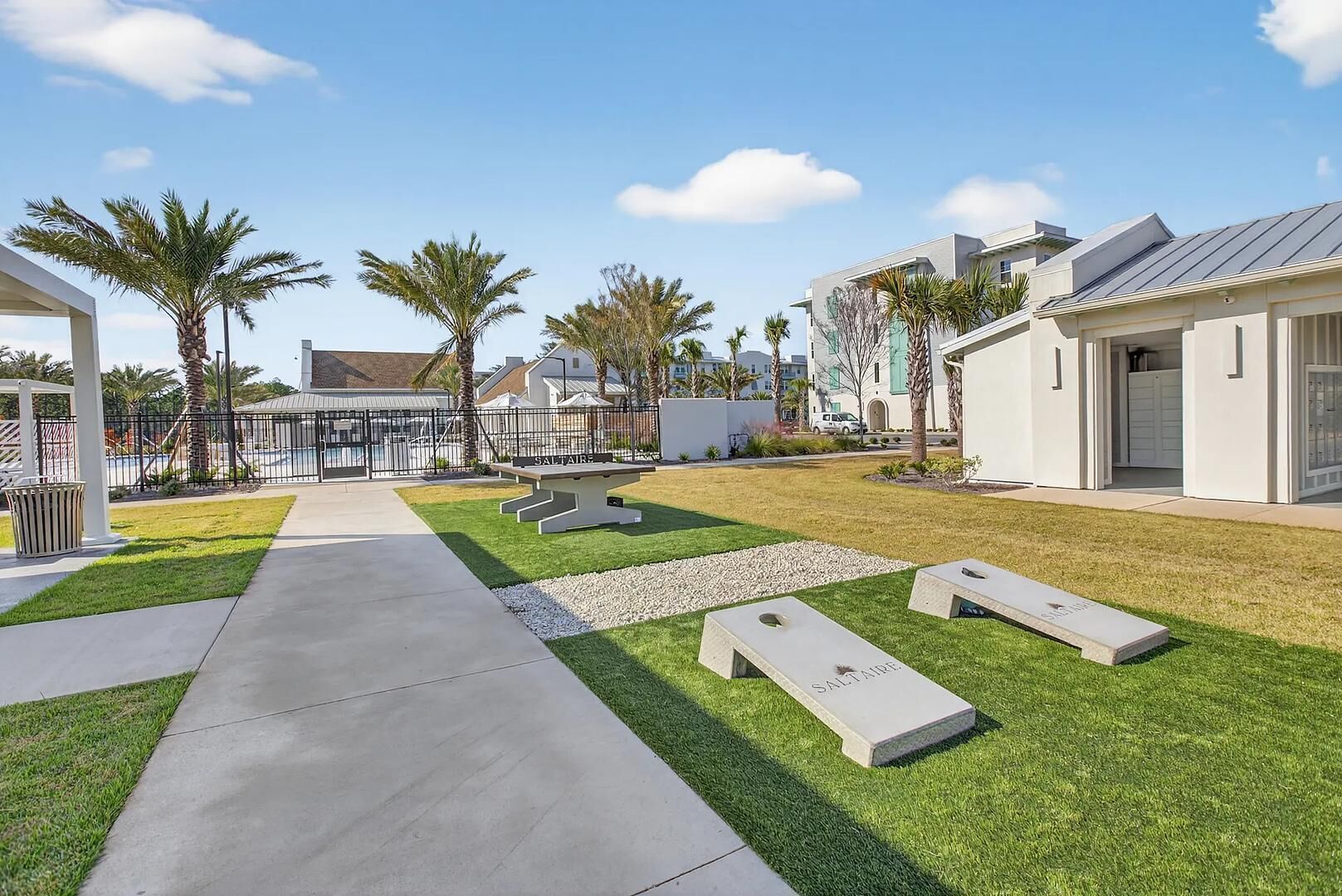 Zona residencial amb un camí pavimentat, una taula de picnic i un petit jardí amb palmeres.