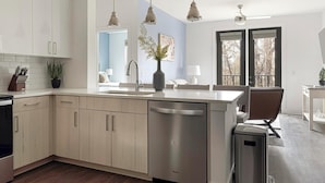 A modern kitchen with a dishwasher, a sink, and a dining area with a chair and table.