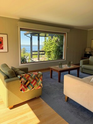 A living room with a large window, a sofa, a coffee table, and a lamp. - Cottage in Jeløy nature reserve with fjord view (Moss)