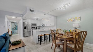 Une cuisine moderne avec des meubles blancs, un îlot central et un coin repas comprenant des chaises et une table en bois.