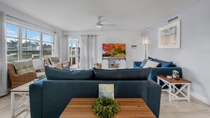 Un salon avec un canapé, une table basse, un ventilateur de plafond, un tableau et une vue par la fenêtre.