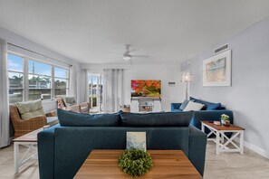 Ein Wohnzimmer mit einer Couch, einem Couchtisch, einem Deckenventilator, einem Gemälde und Blick durch das Fenster.