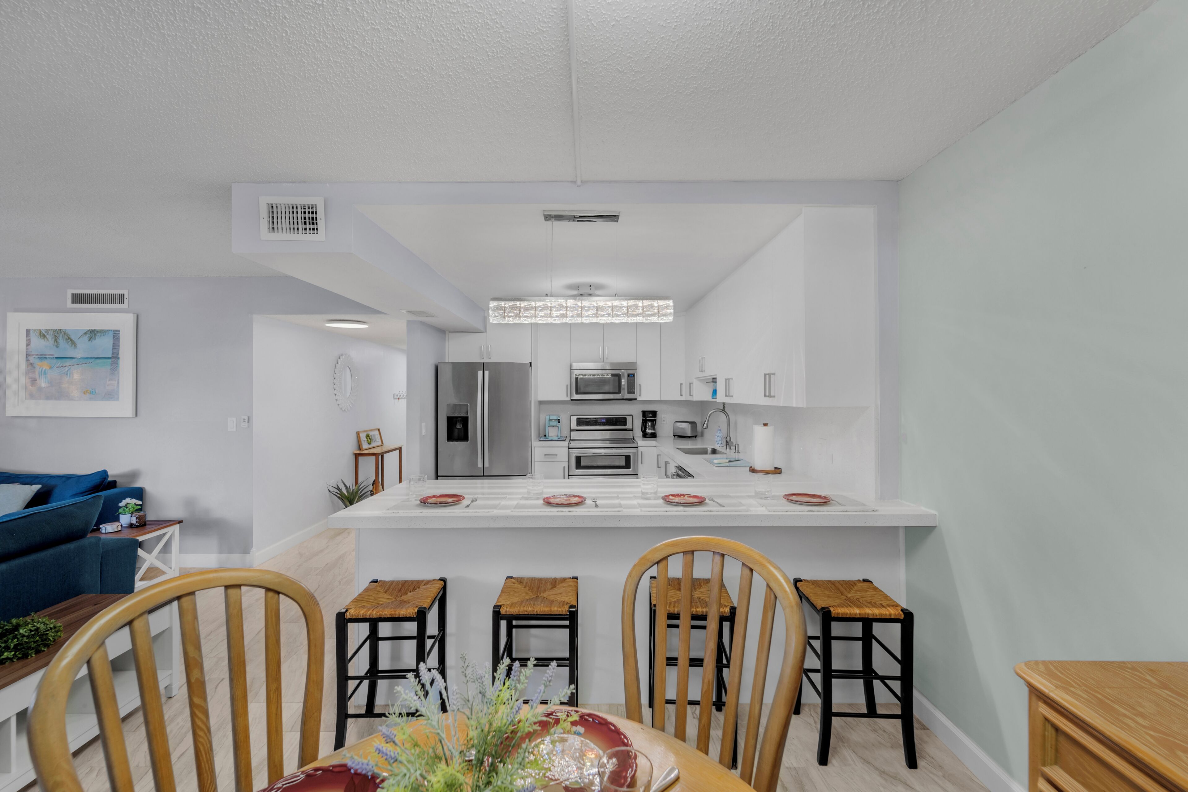 Uma cozinha moderna com armários brancos, uma ilha central com banquetas e uma área de jantar com mesa e cadeiras de madeira.