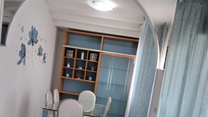 Ein Wohnzimmer mit einem schwarzen Ledersofa, einem Esstisch mit Stühlen, einem Bücherregal und einer Wand mit blauen Blumenmustern.