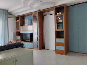 Ein Zimmer mit integriertem Fernseher, einem Schrank mit Glastüren und einer Kommode.