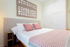 Ein Schlafzimmer mit Bett, Kissen, Nachttisch, Kleiderschrank und einem Wandbild.