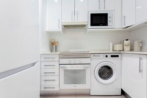 Eine moderne Küche mit weißen Schränken, einer Mikrowelle, einem Backofen und einer Waschmaschine.
