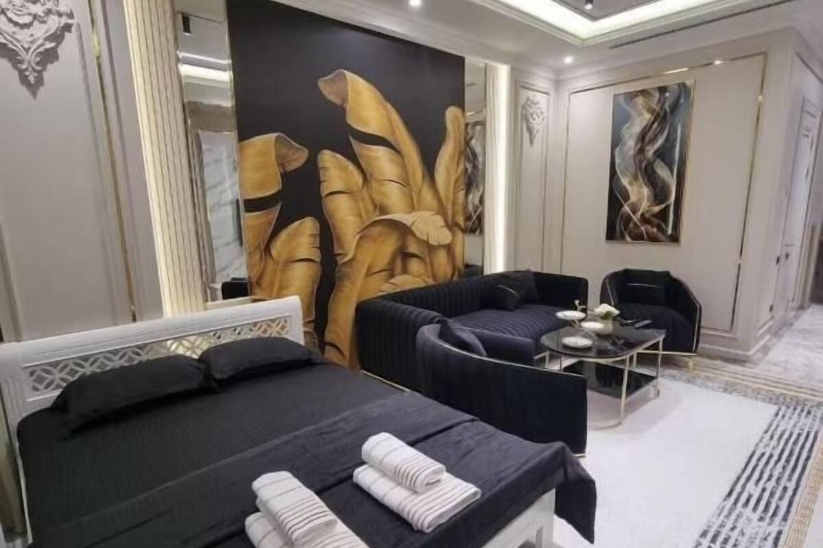 Una habitación de hotel moderna con una cama grande, una zona de estar y una pared con arte abstracto.