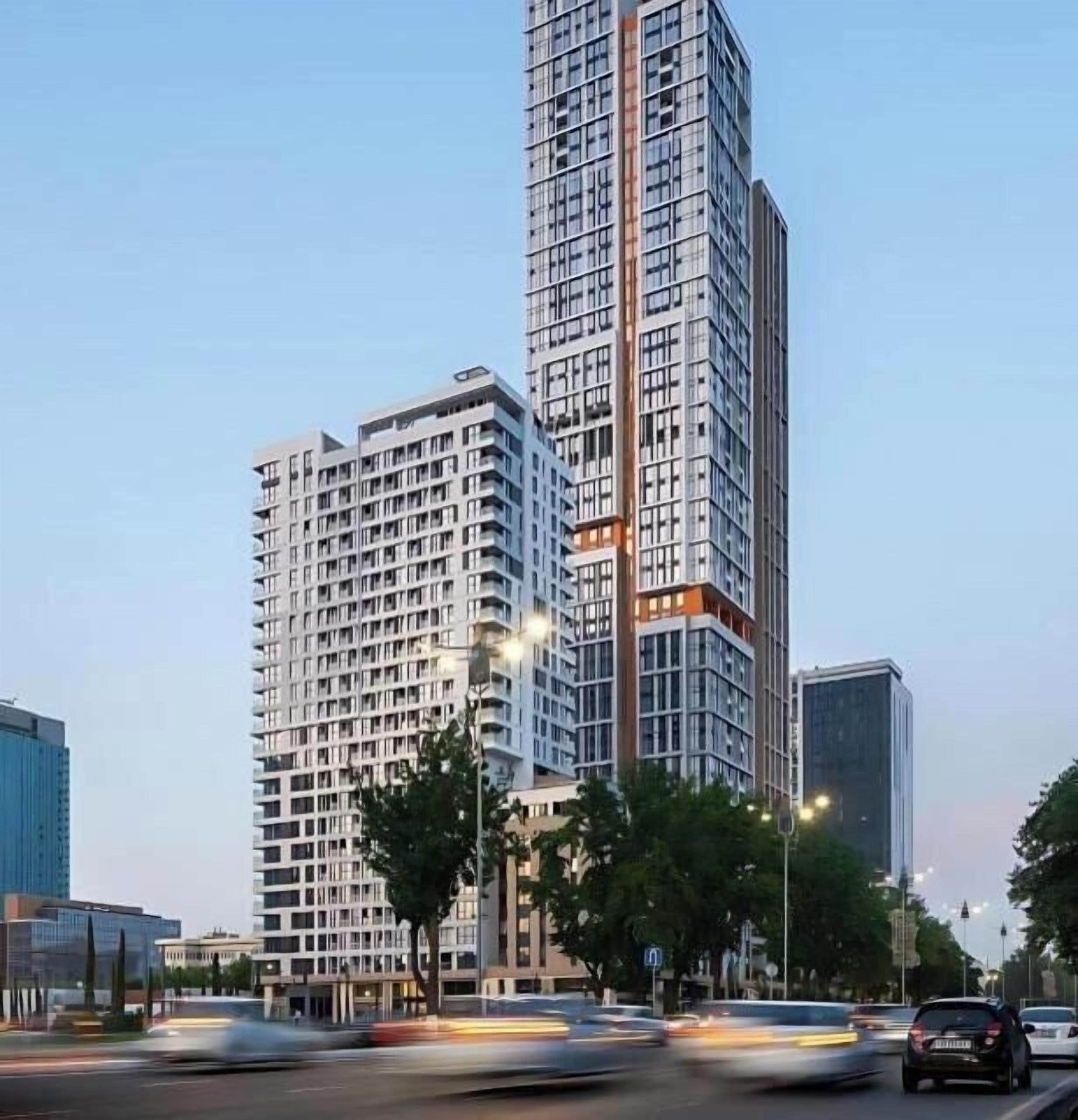 A high-rise building with multiple floors, a clear sky, and a busy street with moving vehicles.