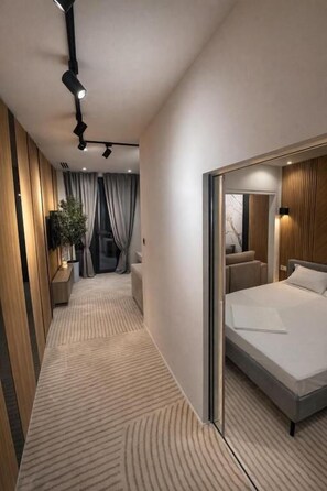 A modern hotel room with a large bed, a mirror, a bedside table, and a plant.