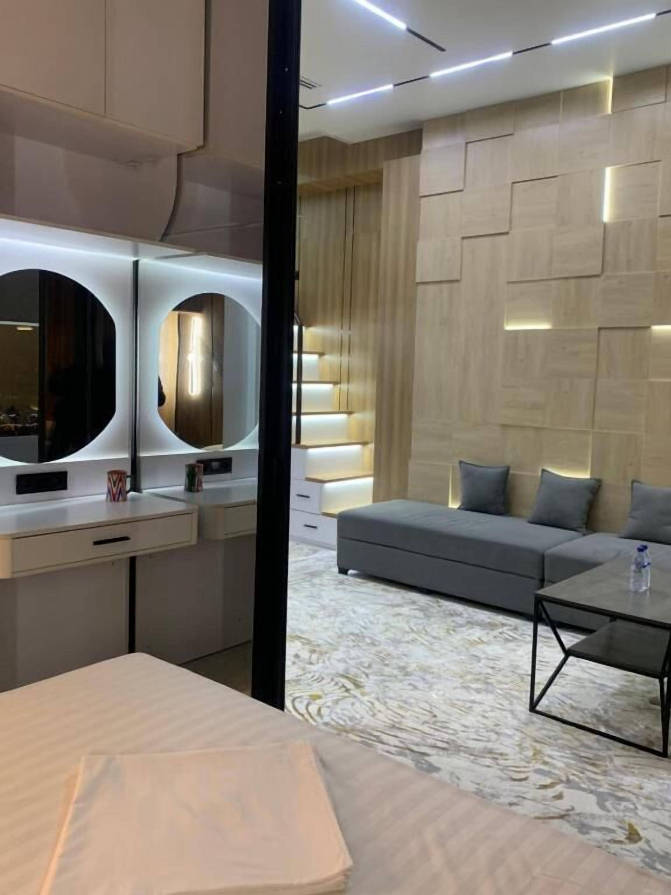 A modern hotel room with a bed, a sofa, a coffee table, and a large mirror.